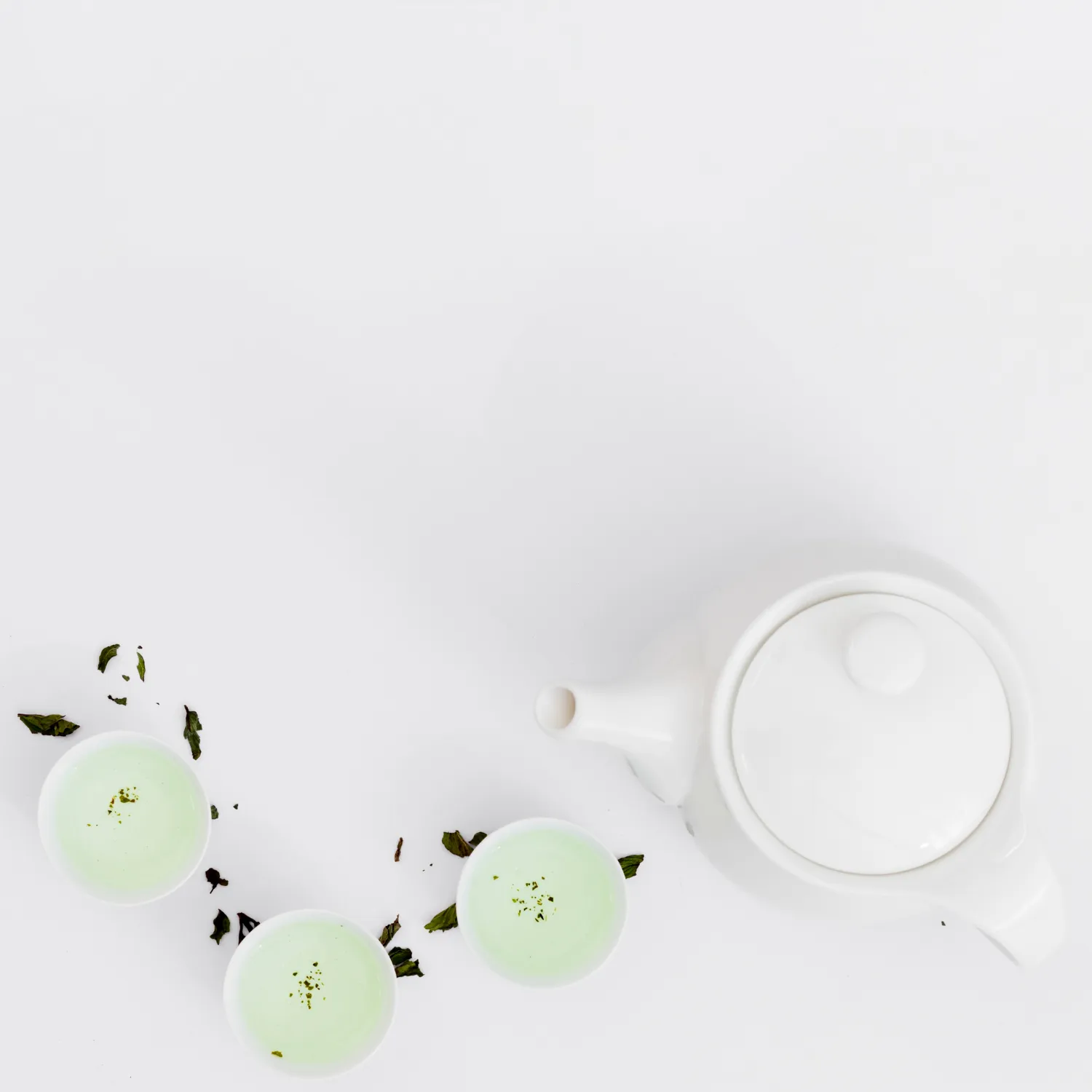 Baltoji arbata mažuose puodeliuose ir keraminis arbatinukas ant balto stalo