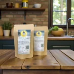 Matcha Kumo Du rudo kraftpopieriaus pakeliai su japoniška matcha arbata „Japan Matcha Kumo“ iš „Tea Haven“, stovintys ant medinio stalo neryškiame virtuvės fone.