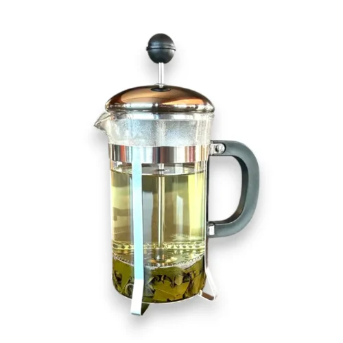 Stiklinis french press kavinukas pilnas žaliosios arbatos baltame fone