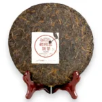 Išpakuotas 357g Haiwan Pu-erh arbatos blynas ant medinio stovo