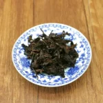 Išsiskleidę tamsūs fermentuoti Pu-erh arbatos lapeliai po plikymo lėkštutėje