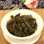 Išsiskleidę žali brandinti Sheng Pu-erh arbatos lapeliai baltame Gaiwan indelyje