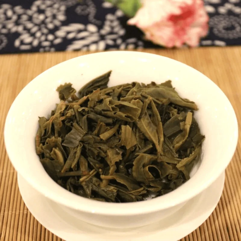 Išsiskleidę žali brandinti Sheng Pu-erh arbatos lapeliai baltame Gaiwan indelyje