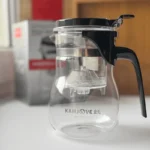 SK00135-02 arbatos plikymo indas su filtru Kamjove K-203 šalia firminės pakuotės